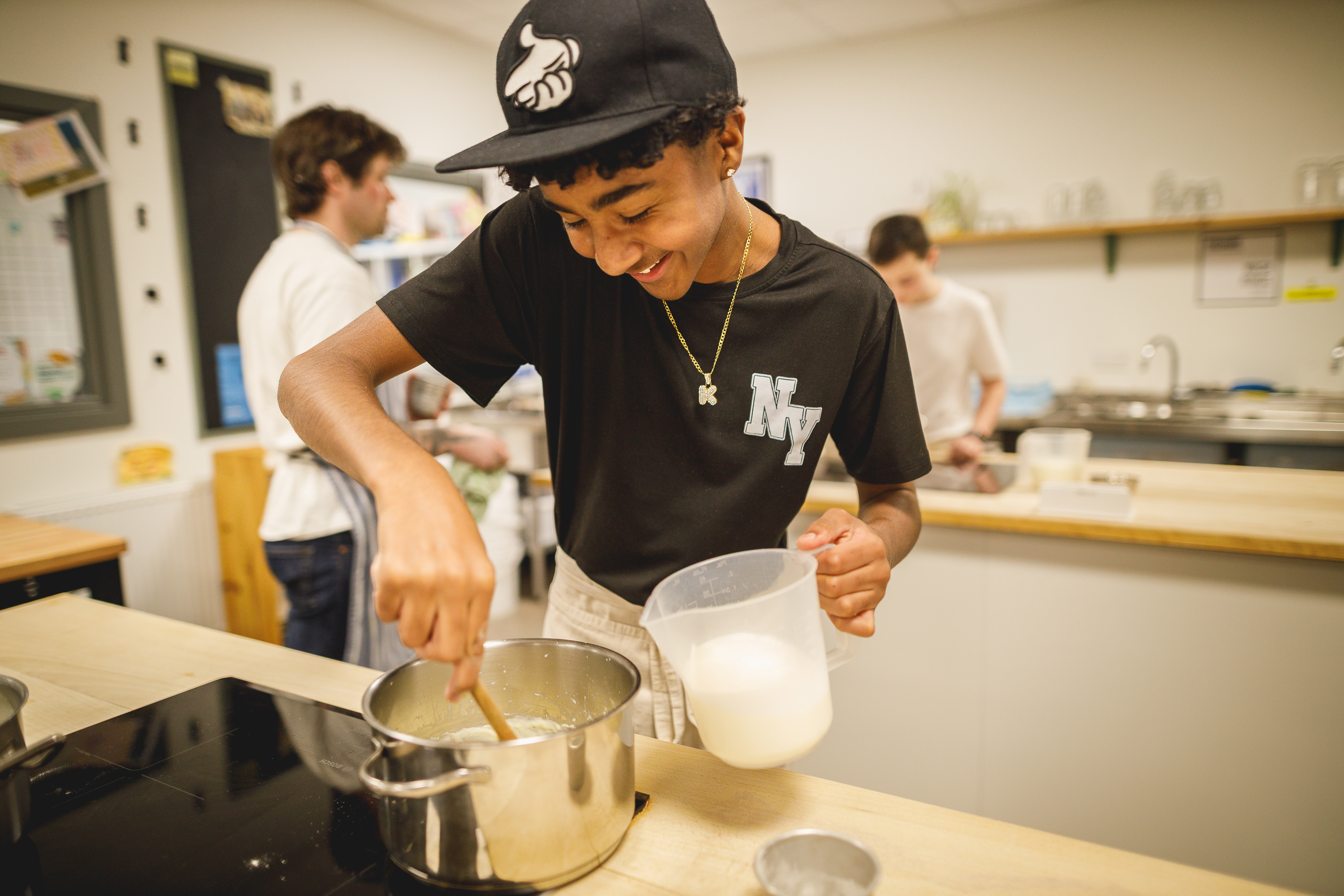 Teenage boy in black cap stirring white sauce in a kitchen.jpg