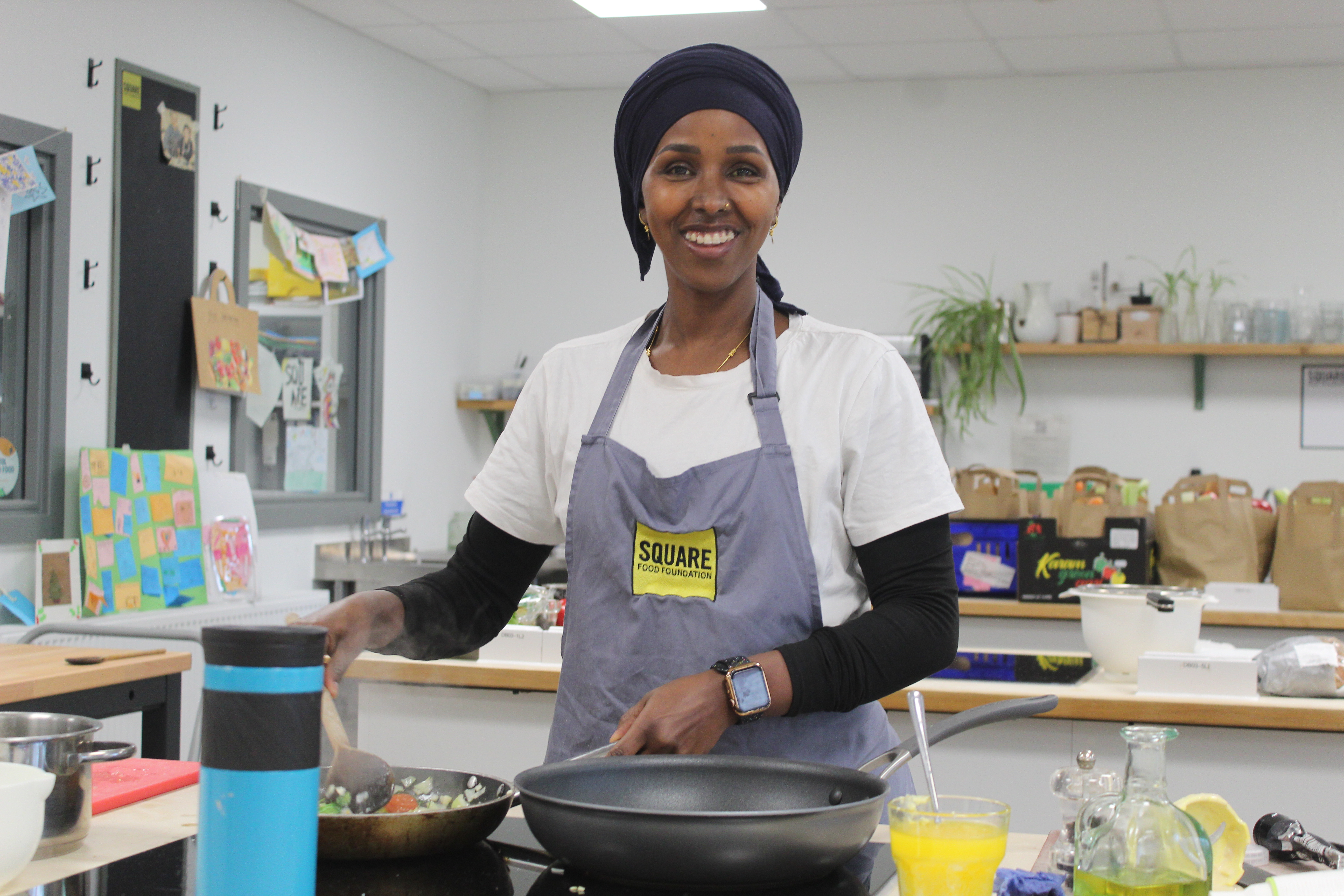 Woman in headscarf and apron cooking in a kitchen with frying pan.JPG