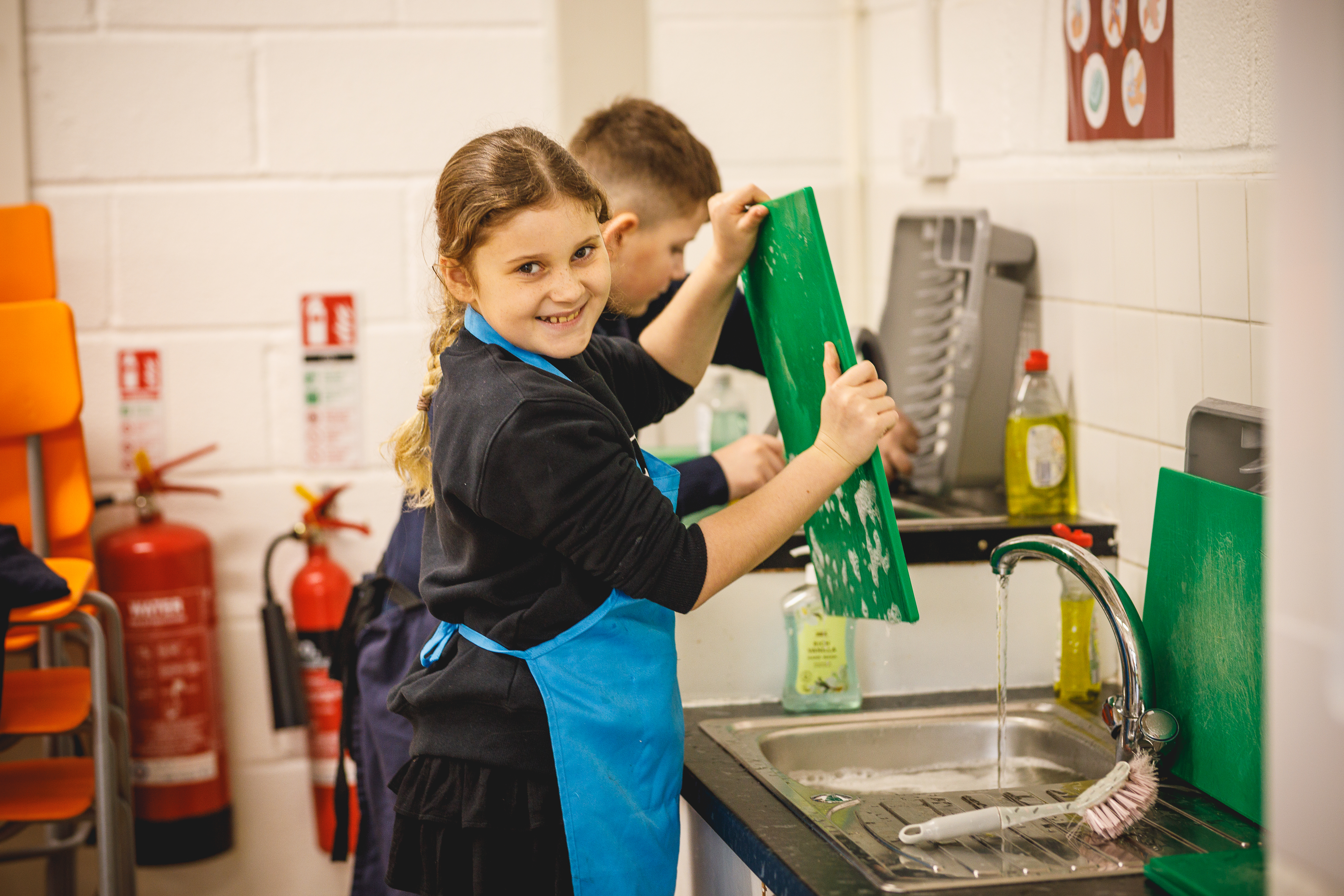 Primary school girl doing washing up and smiling to camera.jpg