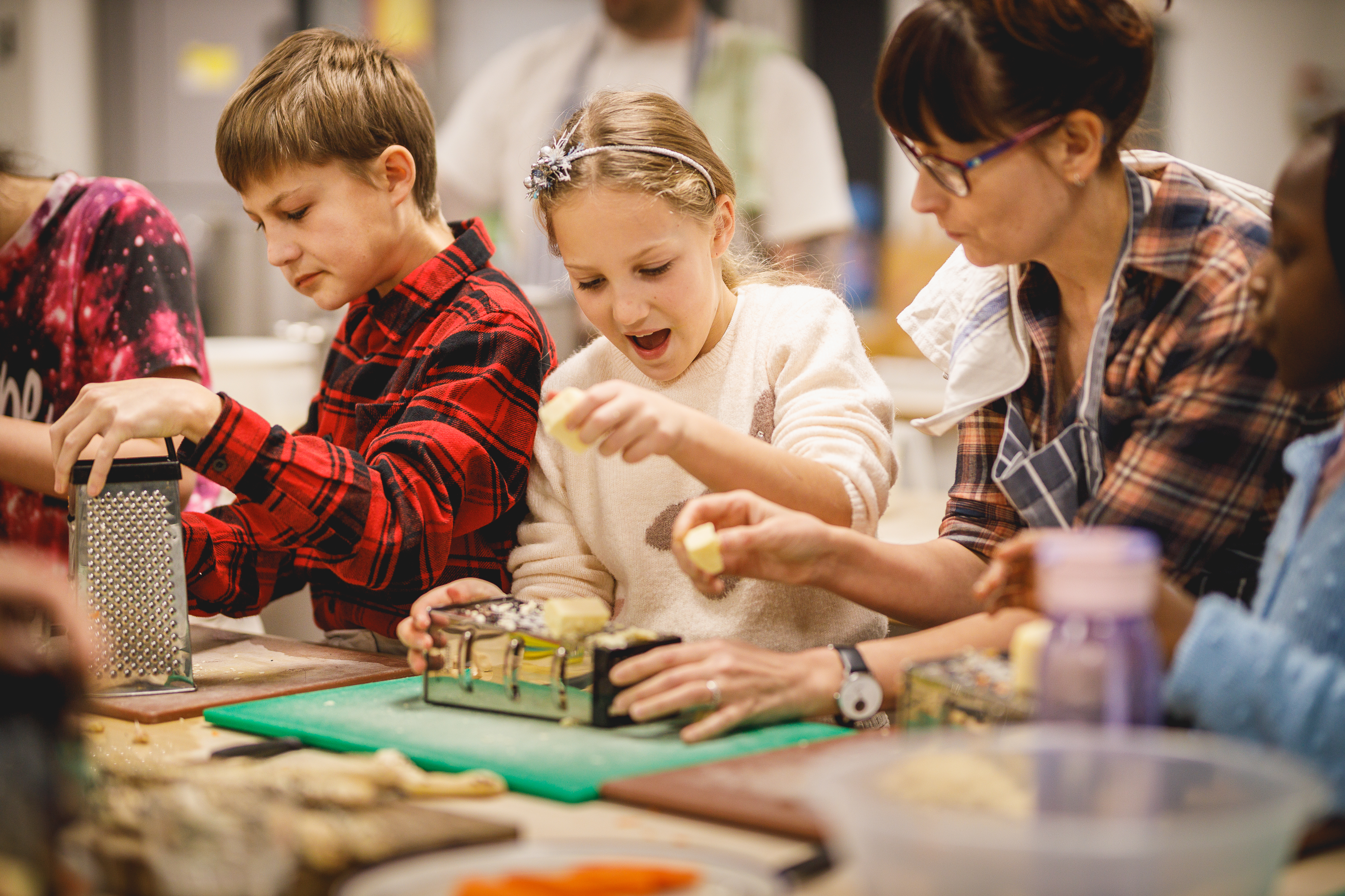 A busy classroom with several children grating cheese and a helper.jpg