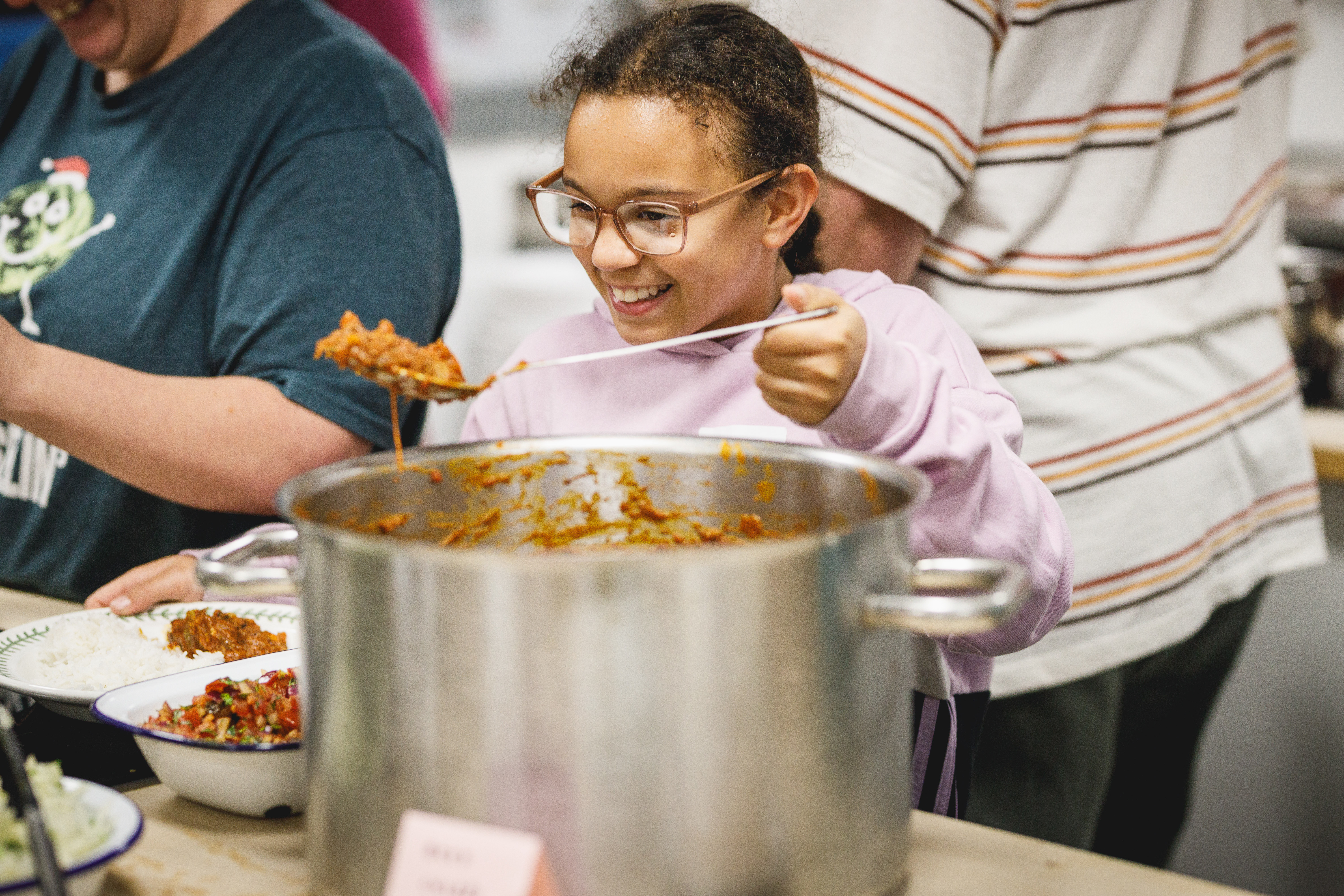 Smiling young girl serving herself food from a big pan.jpg