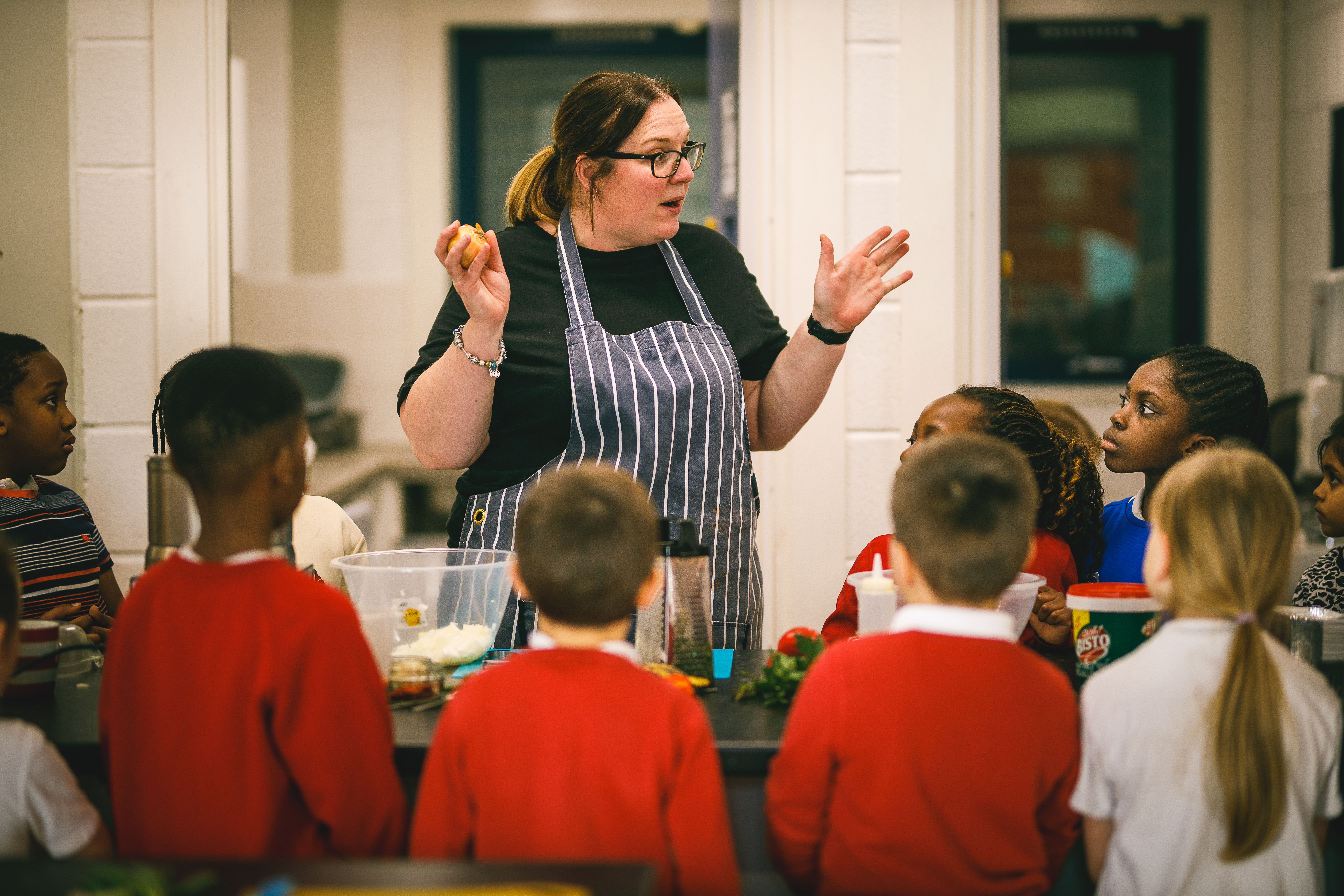 Cookery teacher Lucy talking to a class of kids in red jumpers.jpg