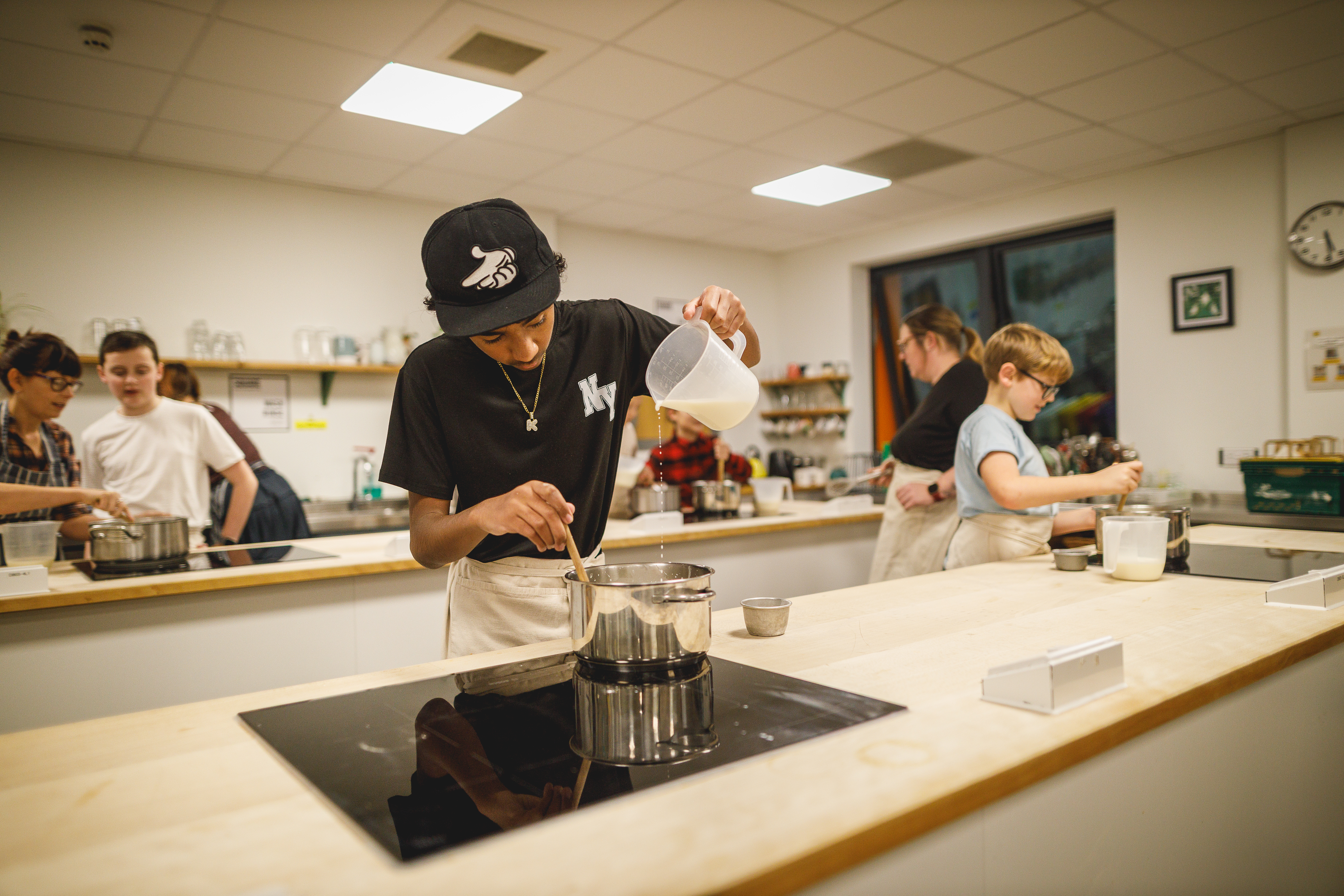 Teenage boy in a black cap pouring liquid from a jug into a pan.jpg