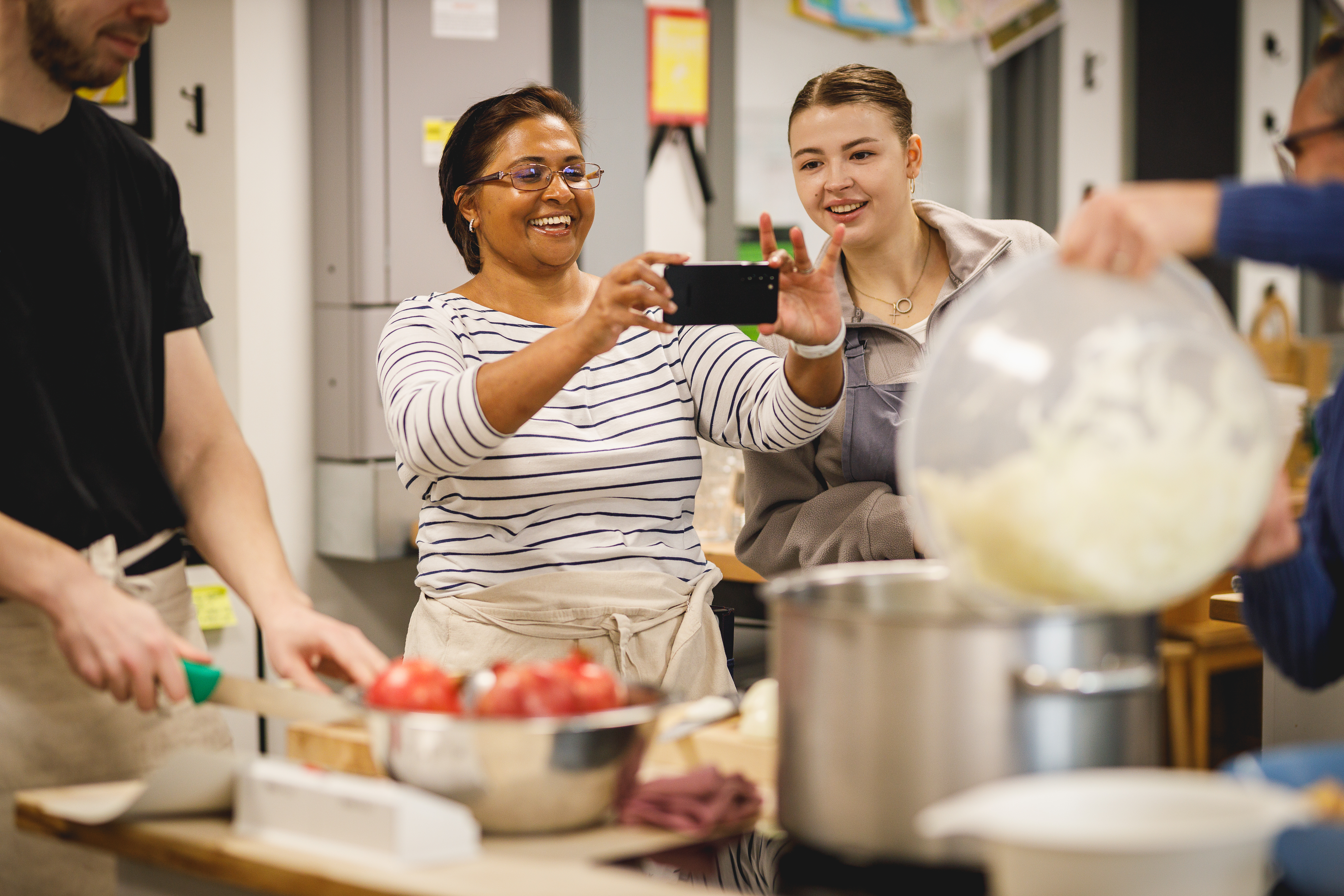 Smiling woman taking a photo on her phone during a cookery class.jpg