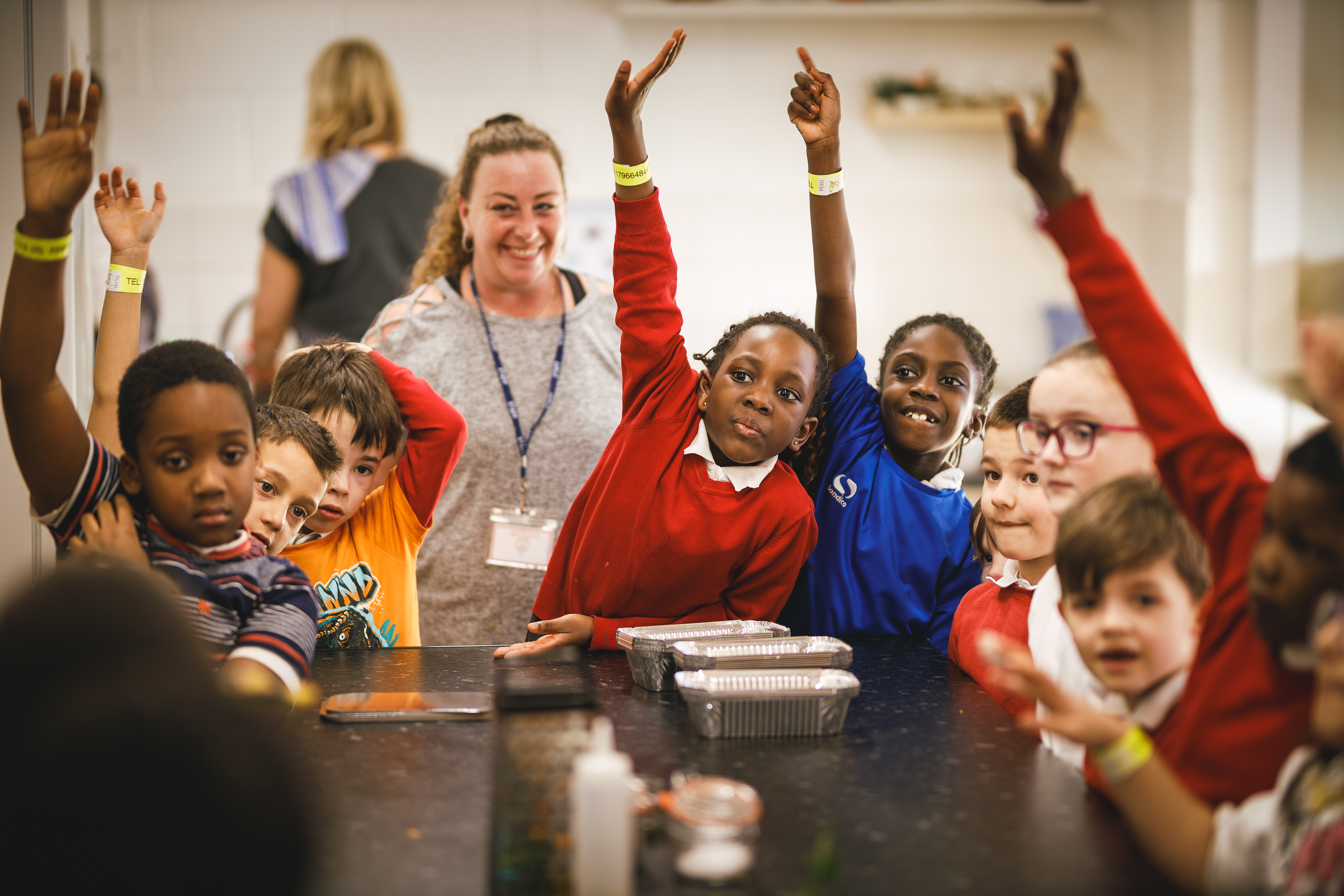 A classroom full of children with their hands enthusiastically in the air.jpg