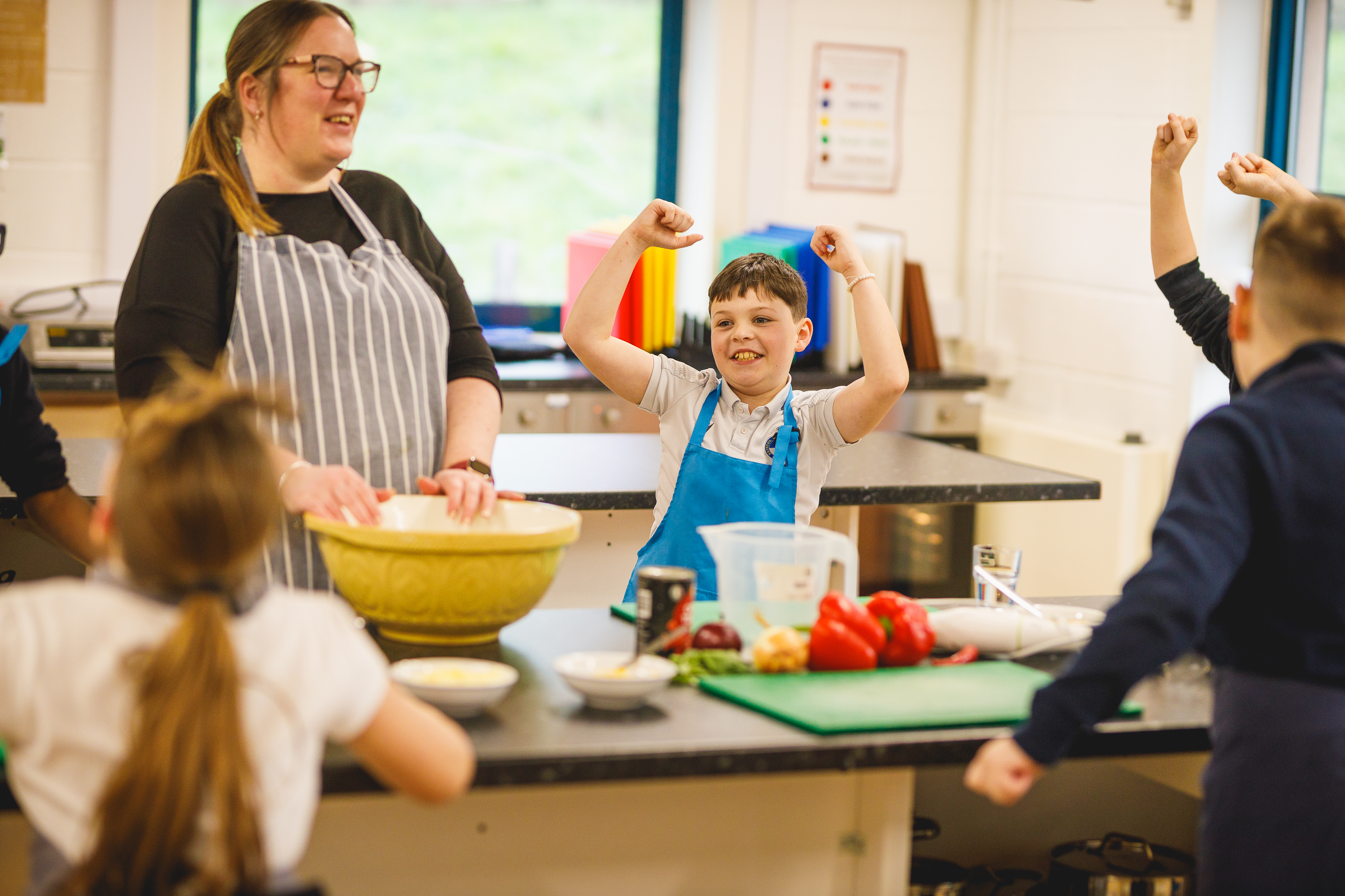 School boy cheering in kitchen with teacher looking pleased.jpg