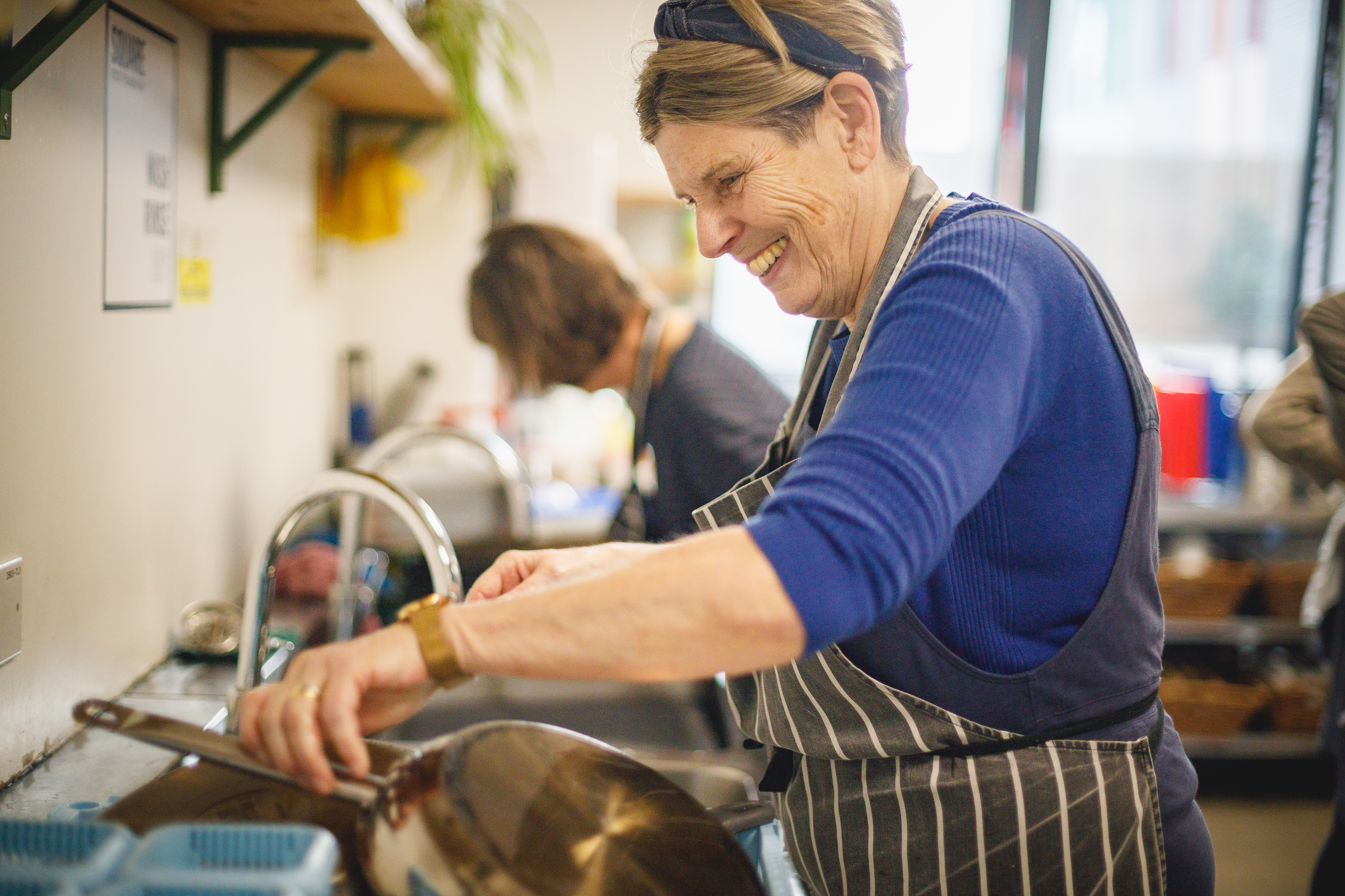 Smiling volunteer in a blue jumper washing up pans.jpg