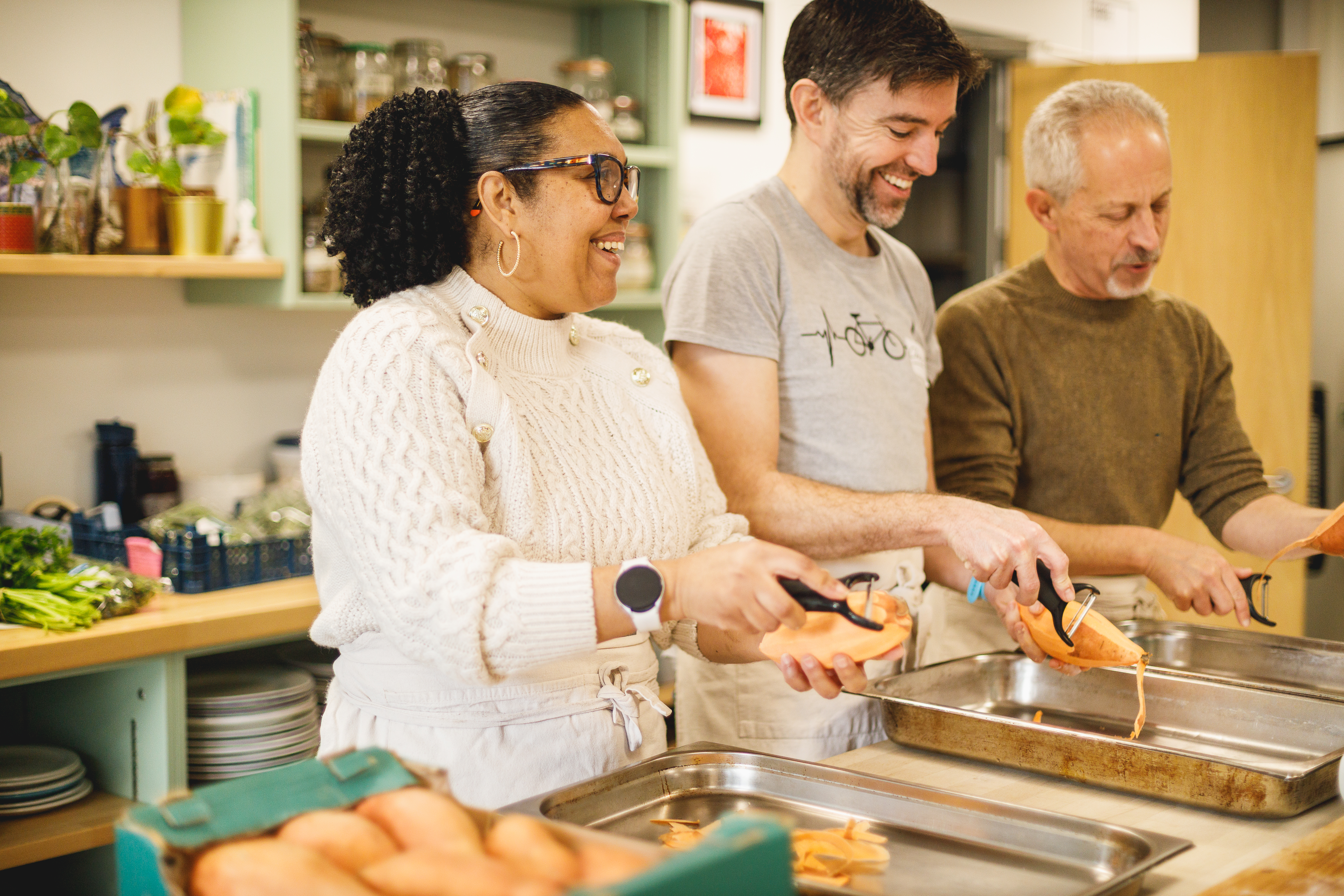 Three people in the cookery kitchen peeling sweet potatoes together.jpg